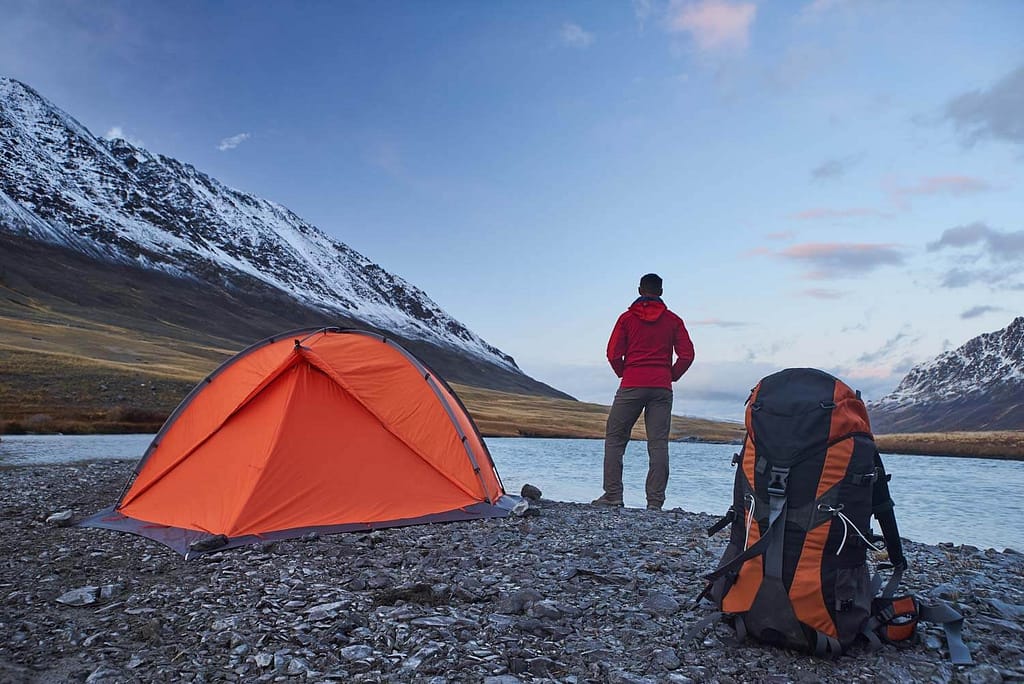 backpacker standing at lake by tent