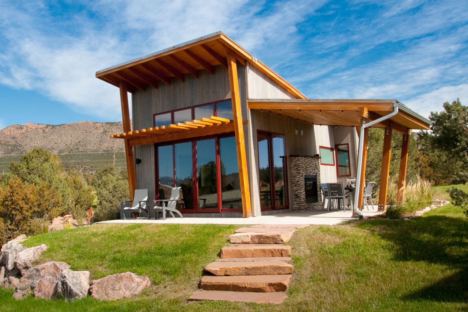 Modern cabin with large windows and slanted roof set in a scenic mountain landscape.
