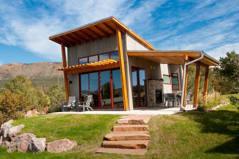 Modern cabin with large windows and slanted roof set in a scenic mountain landscape.