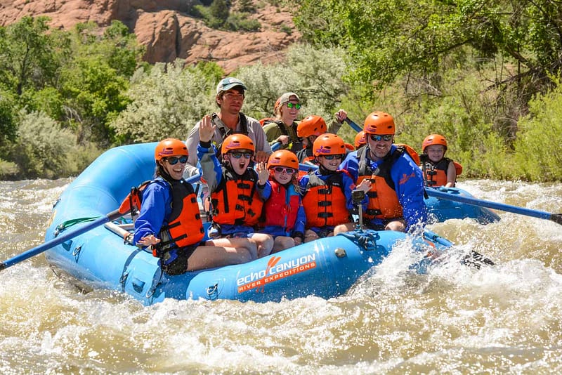 A family wearing helmets and life jackets, having fun rafting through mild rapids with a guide