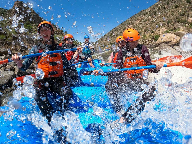 Rafters are splashed by a large wave as they paddle a class IV rapid