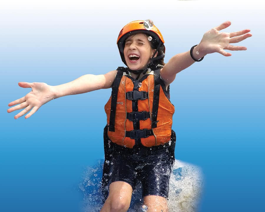 Young girl in rafting gear with arms out, smiling as water splashes over the raft